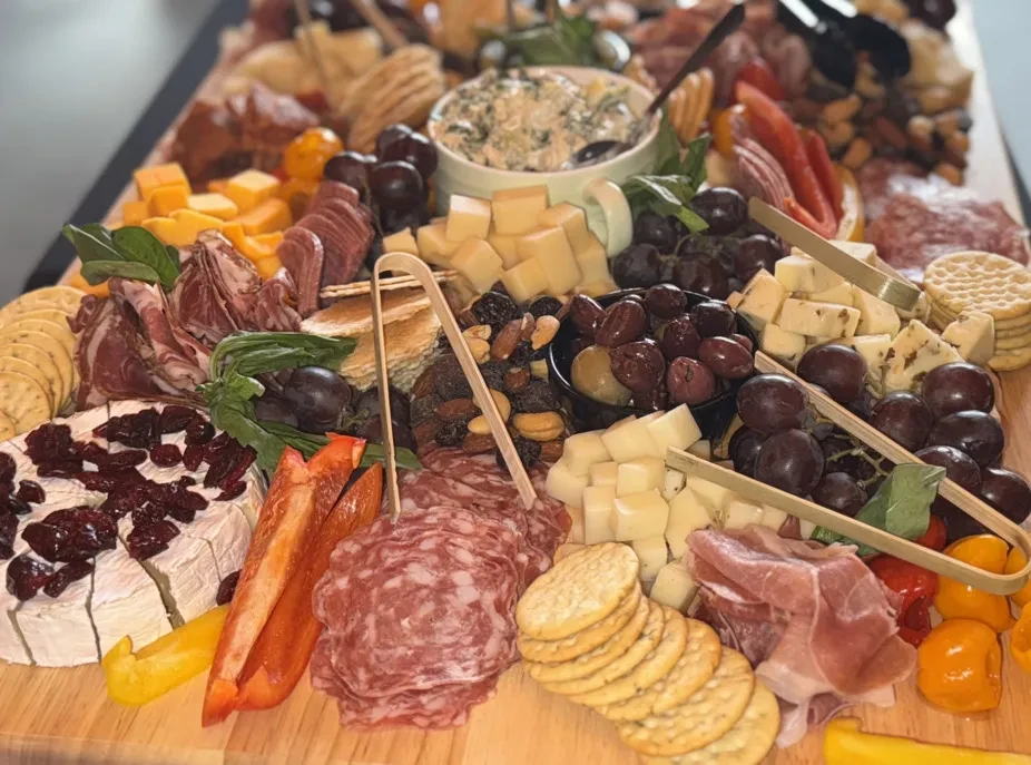 Charcuterie board overflowing with cheeses, meats, fruits, vegetables, crackers, and dip.