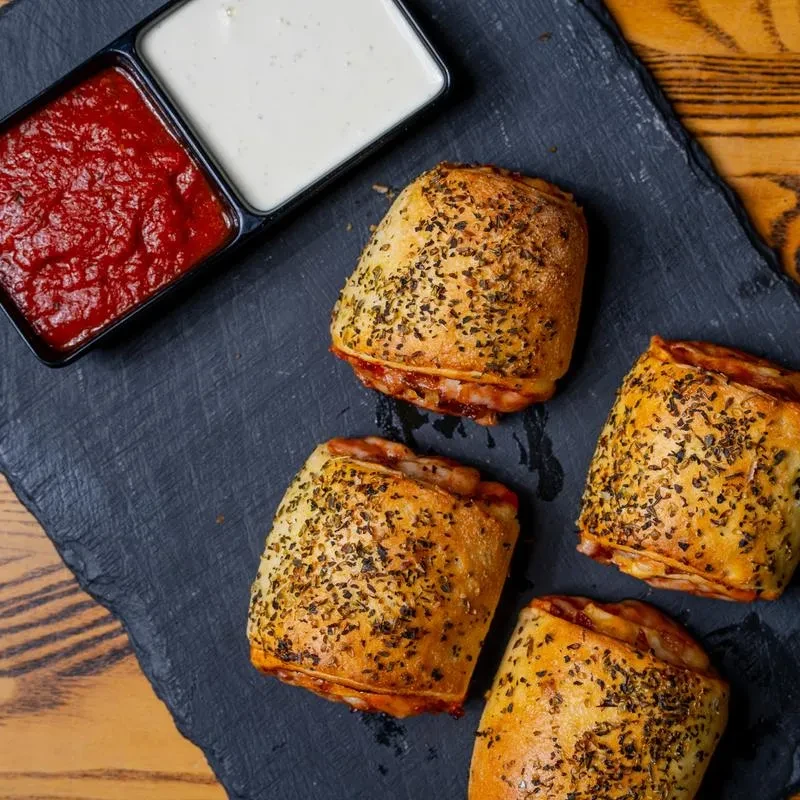 Four herb-sprinkled golden pizza rolls with red and white dipping sauces.