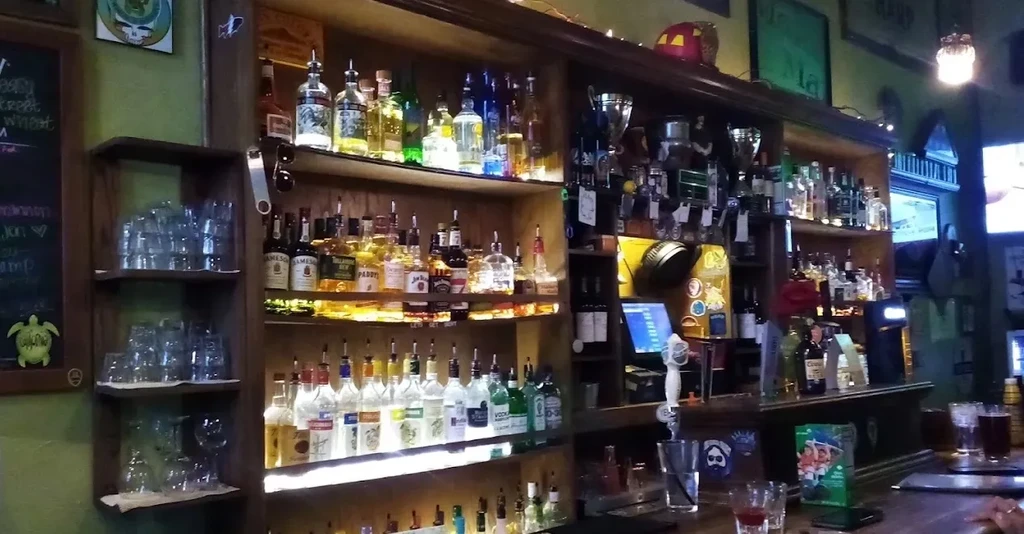 A well-lit, well-stocked bar counter with liquor shelves, beer taps, and drinks.