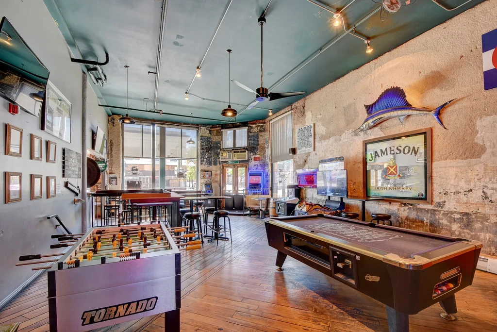 Empty bar interior with foosball, pool table, arcade, and TVs.
