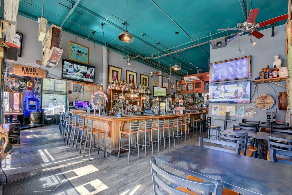 Well-stocked bar interior with a long wooden counter and teal ceiling.