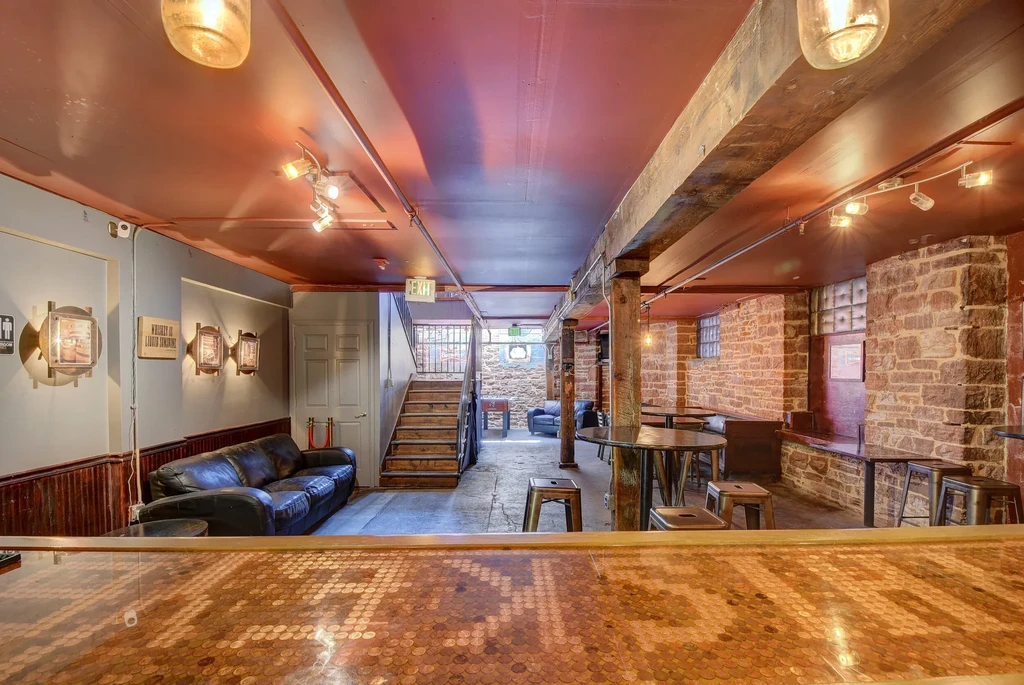 Rustic bar interior with copper penny counter, stone walls, and warm lighting.