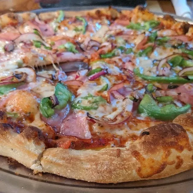 Freshly baked pizza with ham, peppers, onions, and stretching cheese.