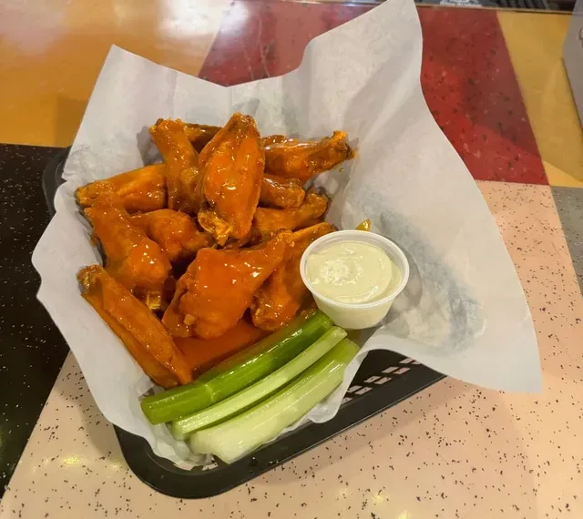 Basket of orange buffalo wings, celery, and dip on speckled table.