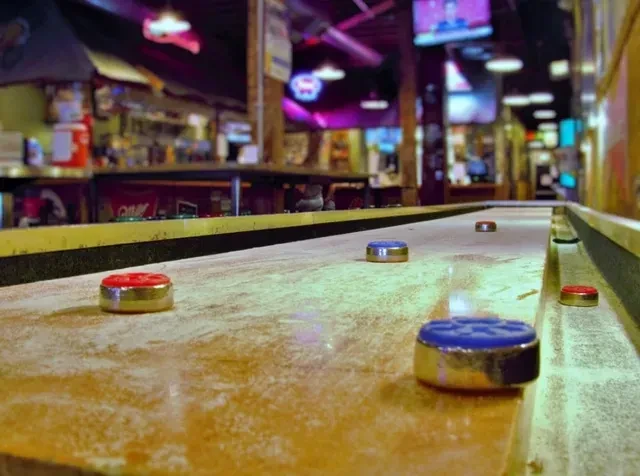 Shuffleboard pucks on a wooden table, with a blurred bar behind.