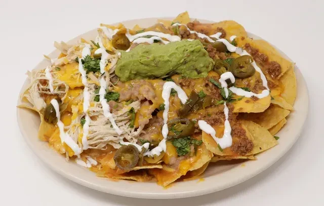 Top-down close-up of fully loaded nachos with cheese, meats, beans, guacamole.