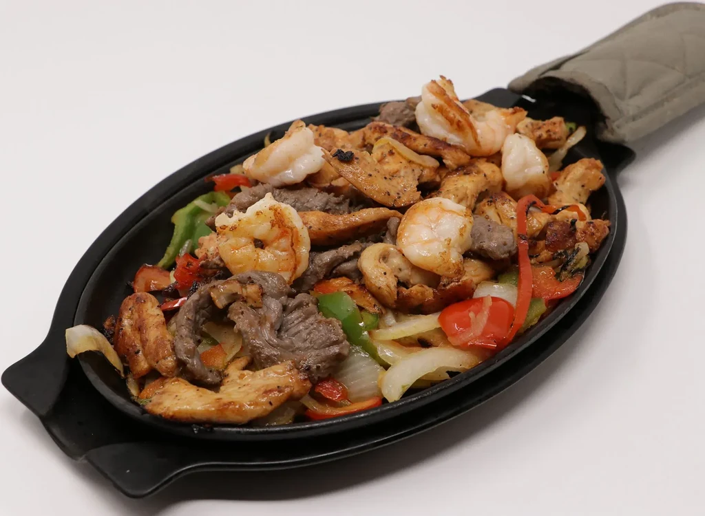 Sizzling shrimp, chicken, beef fajitas with vegetables in a skillet.