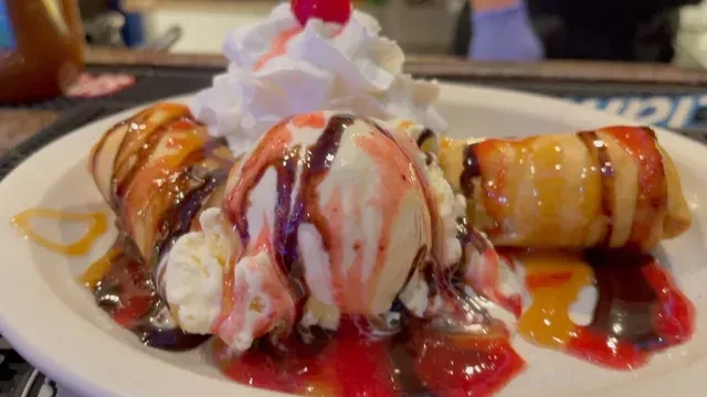 Dessert with deep-fried rolls, melting ice cream, whipped cream, and multiple drizzles.