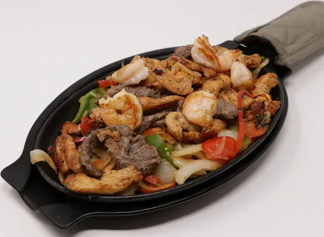 Sizzling shrimp, beef, chicken fajitas with peppers and onions in skillet.