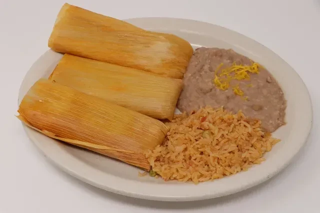 Three tamales, refried beans, and Spanish rice on a white plate.