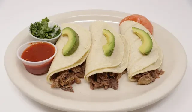 Three soft tacos with shredded meat, avocado, salsa, and cilantro.