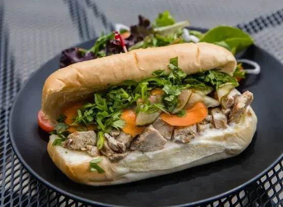 Banh Mi sandwich with meat, pickled vegetables, herbs, and a side salad.