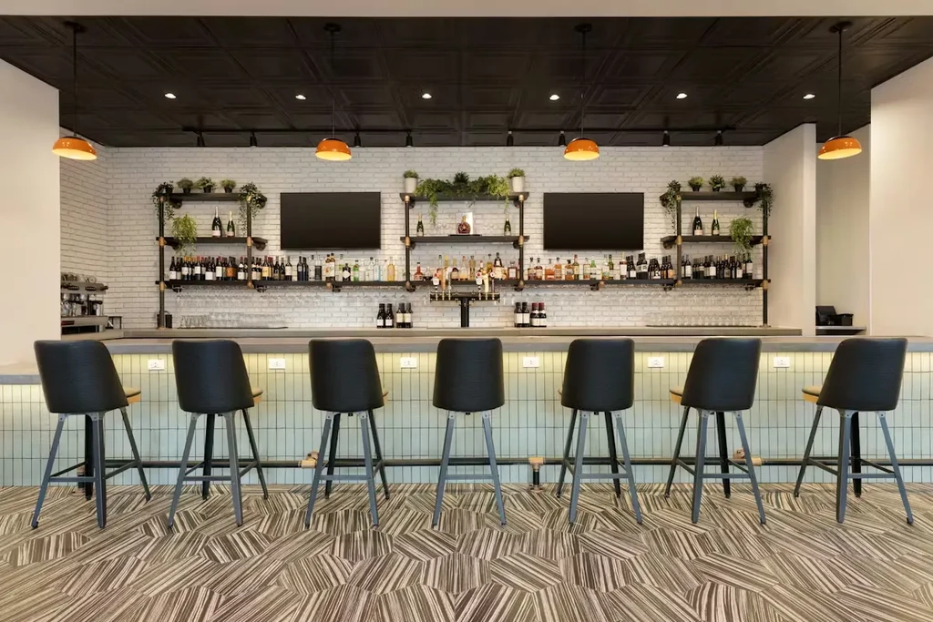 Modern bar area with stocked shelves, warm lighting, and seven bar stools.