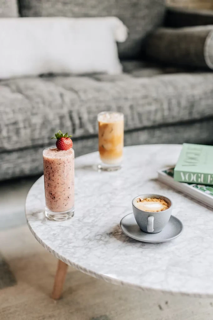 Pink smoothie, latte, iced drink, and Vogue book on table.