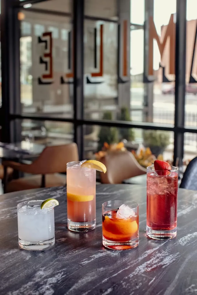 Four distinct cocktails on a dark table, blurred modern interior.