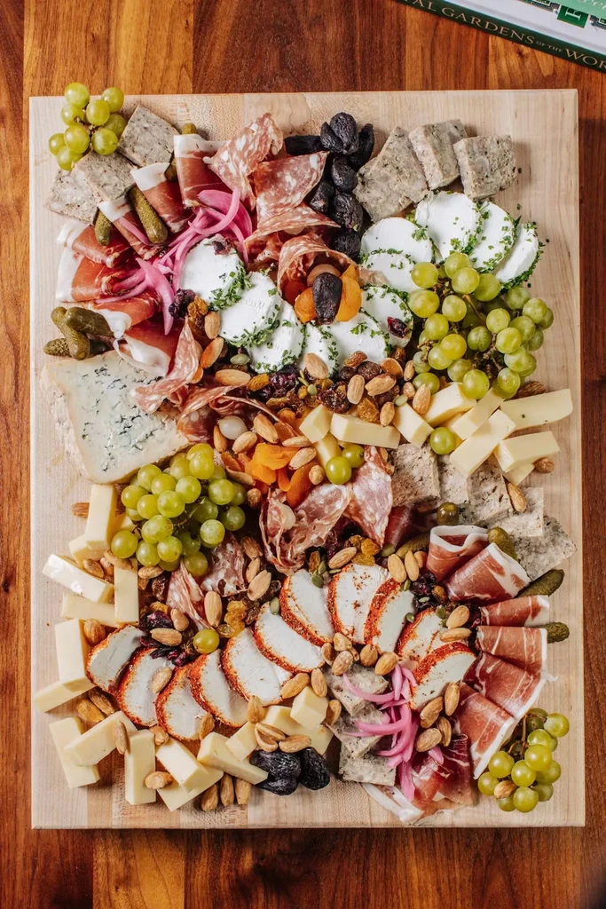 Overhead charcuterie and cheese board with meats, cheeses, fruits, and nuts.