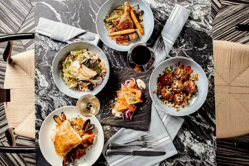 Overhead shot of several gourmet dishes and wine on a marble table.