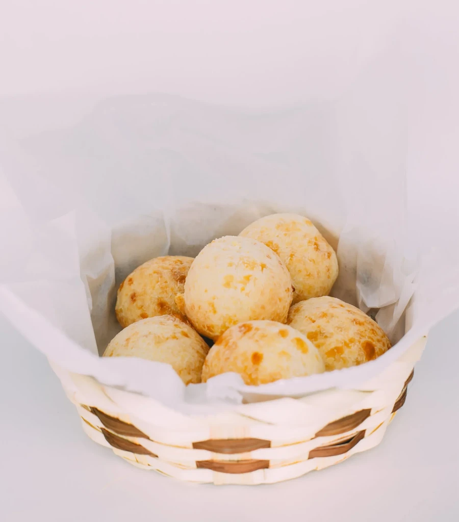 Woven basket of golden-brown cheese bread on white background.