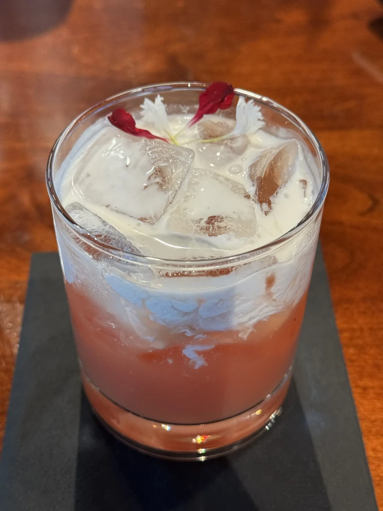 Layered iced drink with peach-orange and creamy white, garnished with petals.