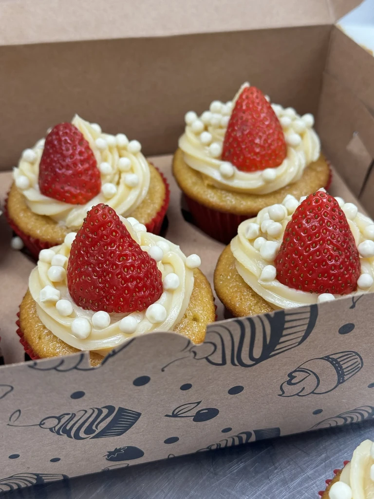 Four cupcakes with strawberry and sprinkles in a light brown box.