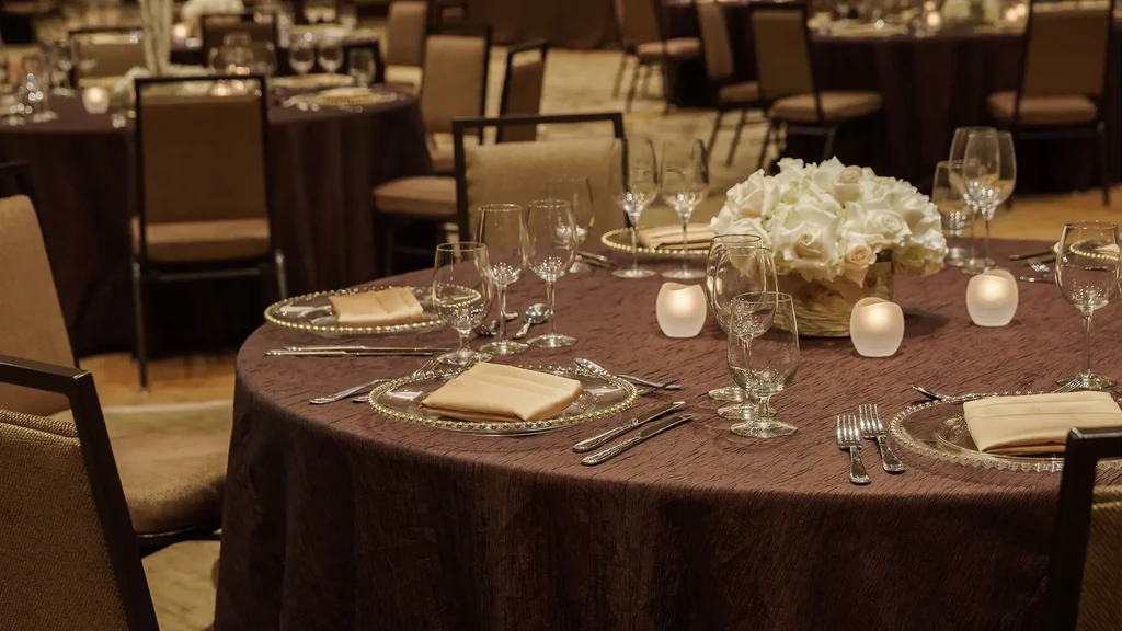 Round dining table formally set with white rose centerpiece and candles.