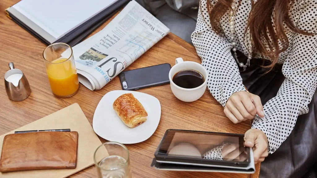 Overhead view of hands, breakfast items, and tablet on wooden table.