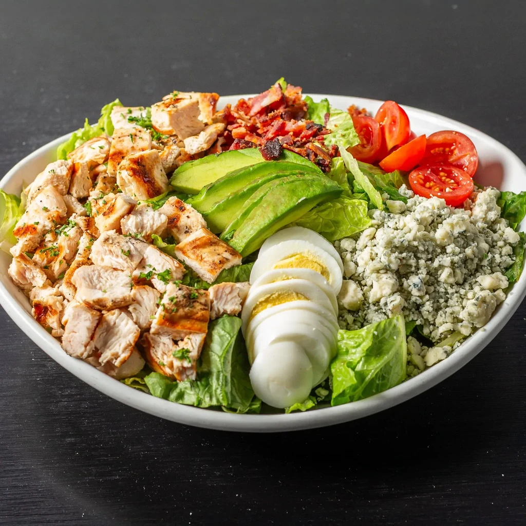 Vibrant grilled chicken salad with avocado, egg, tomato, and blue cheese.