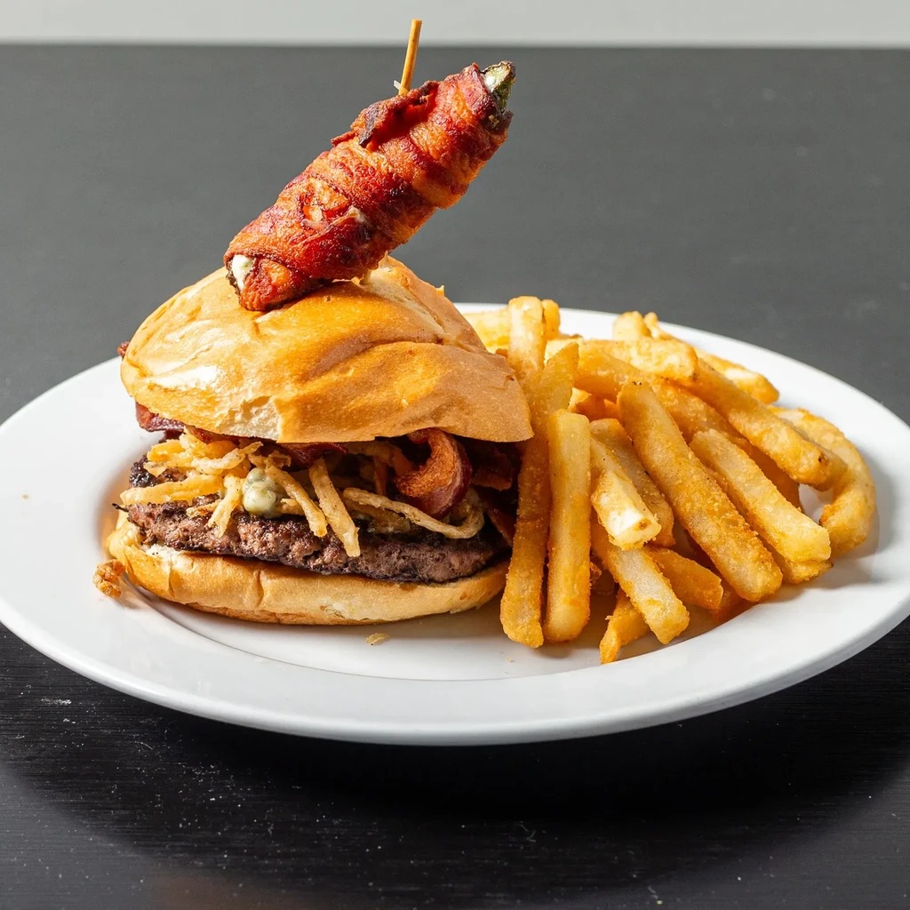 Gourmet burger topped with a bacon-wrapped jalapeño popper and fries.