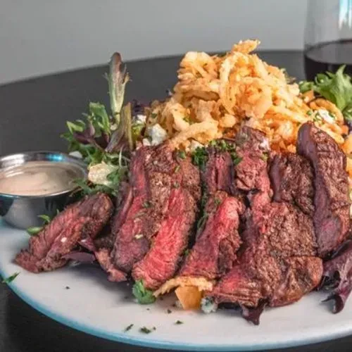 Sliced medium-rare steak salad topped with crispy onions and dressing.