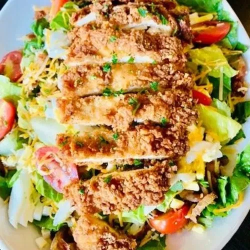 Plate of crispy breaded chicken salad with greens, cheese, and tomatoes.