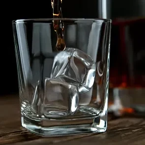 Dark amber liquid actively being poured into clear glass with ice.
