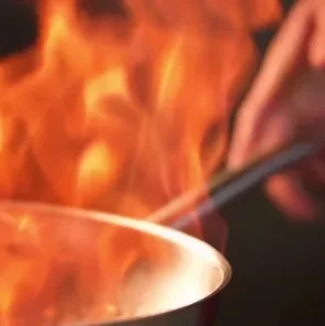Metallic pan held by hand, engulfed in bright orange-yellow flames.
