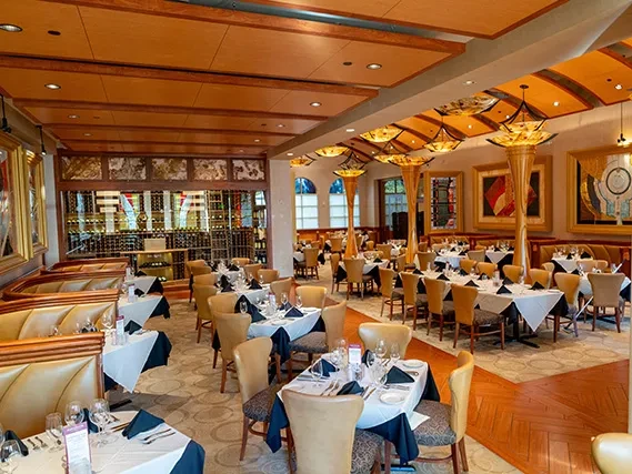 Empty, elegant restaurant dining room with white tablecloths and wine wall.