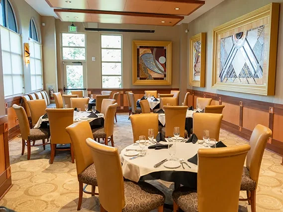 Meticulously set formal dining room with art, wainscoting, and large windows.