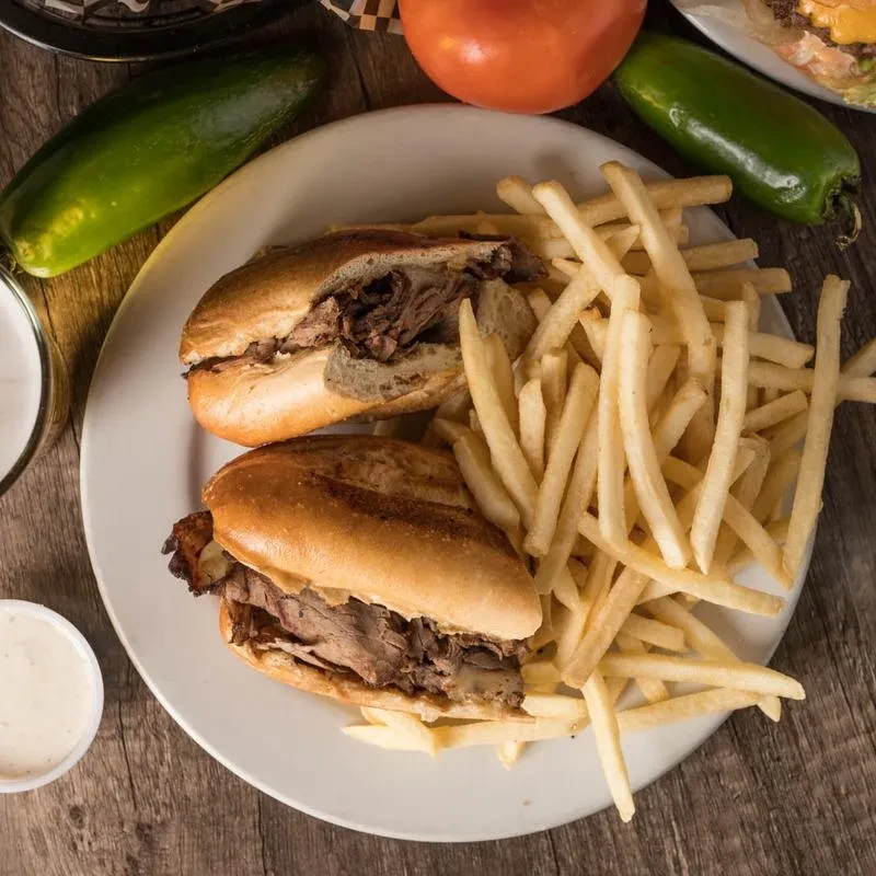 Loaded meat sandwiches, golden fries, creamy sauce, and peppers on wooden table.