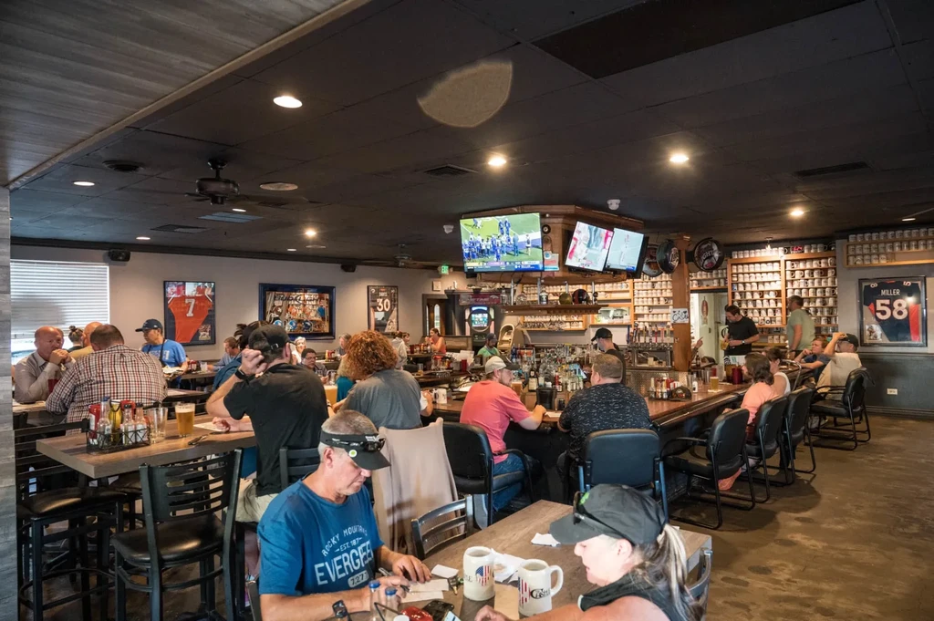 Bustling sports bar interior with patrons, prominent bar, and sports TVs.