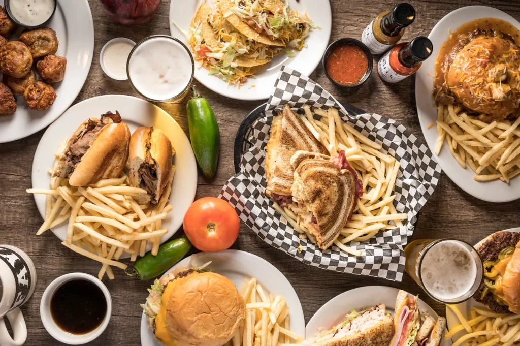 Overhead spread of diverse American comfort foods and drinks on wood.