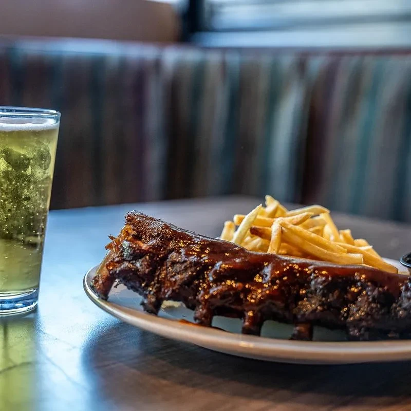 Glistening barbecued ribs, golden fries, and a sparkling drink on a table.