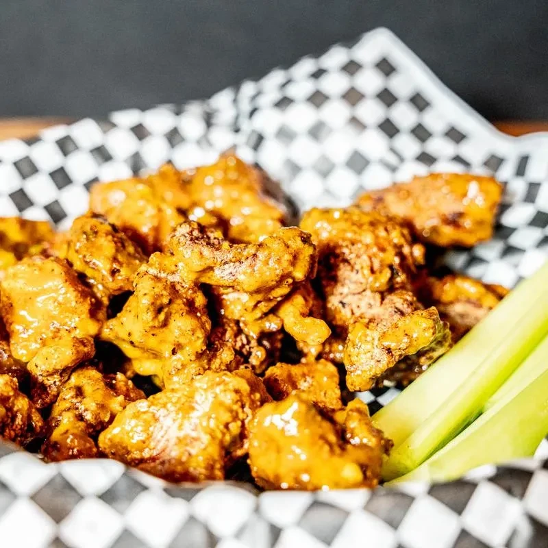 Close-up: Basket of saucy boneless chicken wings with celery sticks.