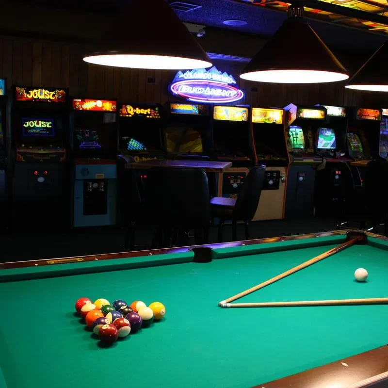 Green pool table, vintage arcade games, and neon signs in a barcade.
