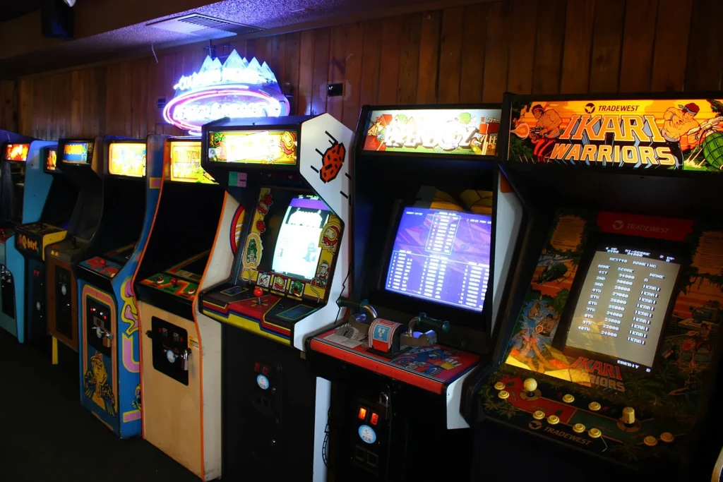 Retro arcade machines glow in a dimly lit, wood-paneled room.
