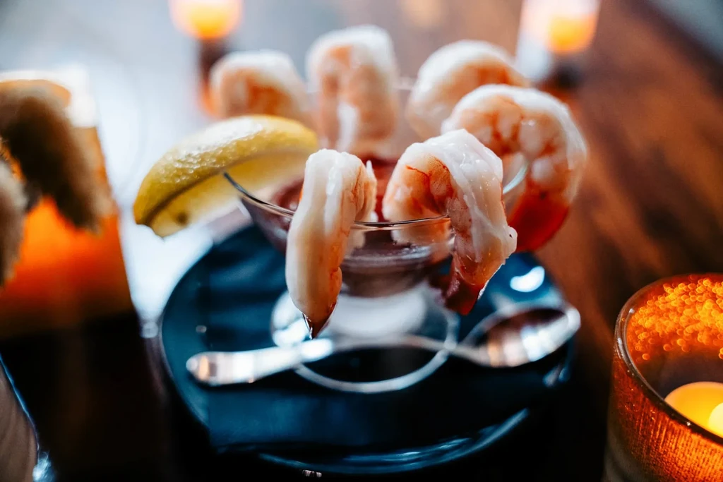 Peeled shrimp cocktail with lemon, red sauce, and candlelit background.