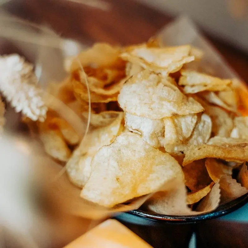 Close-up of golden potato chips, piled high in a dark bowl.