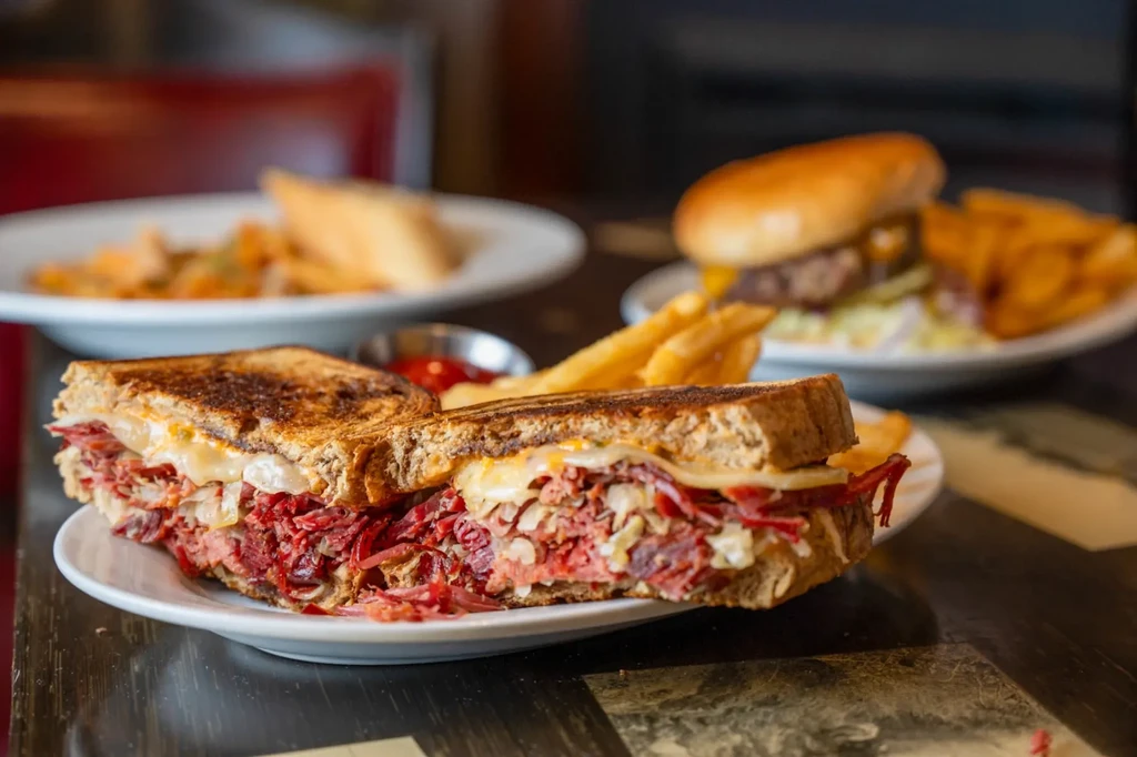 Close-up of a deli sandwich with corned beef, cheese, sauerkraut, and fries.