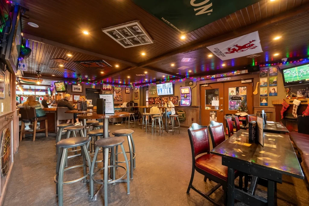 Lively bar interior with patrons, wooden bar, festive lights, and decor.