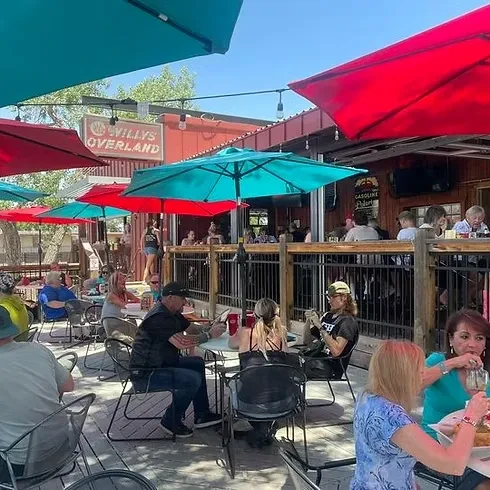 Sunny outdoor patio at Willy's Overland with red/teal umbrellas and diners.