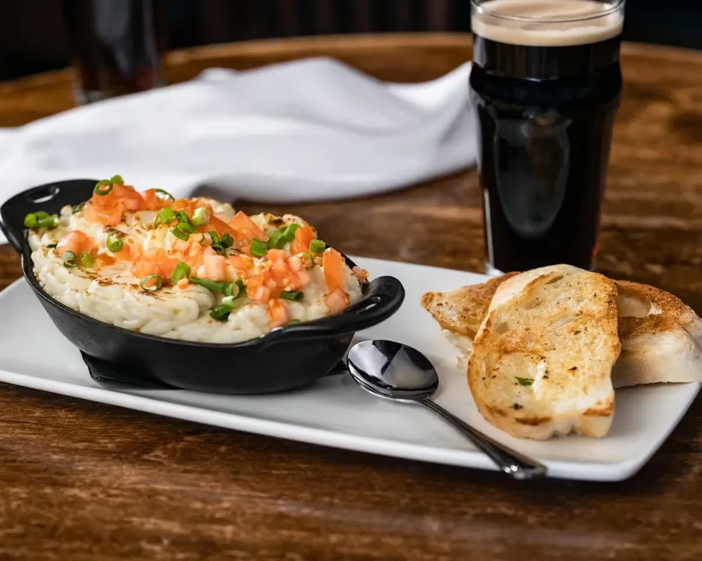 Mashed potatoes with tomatoes, green onions, toasted bread, dark beer on wood.