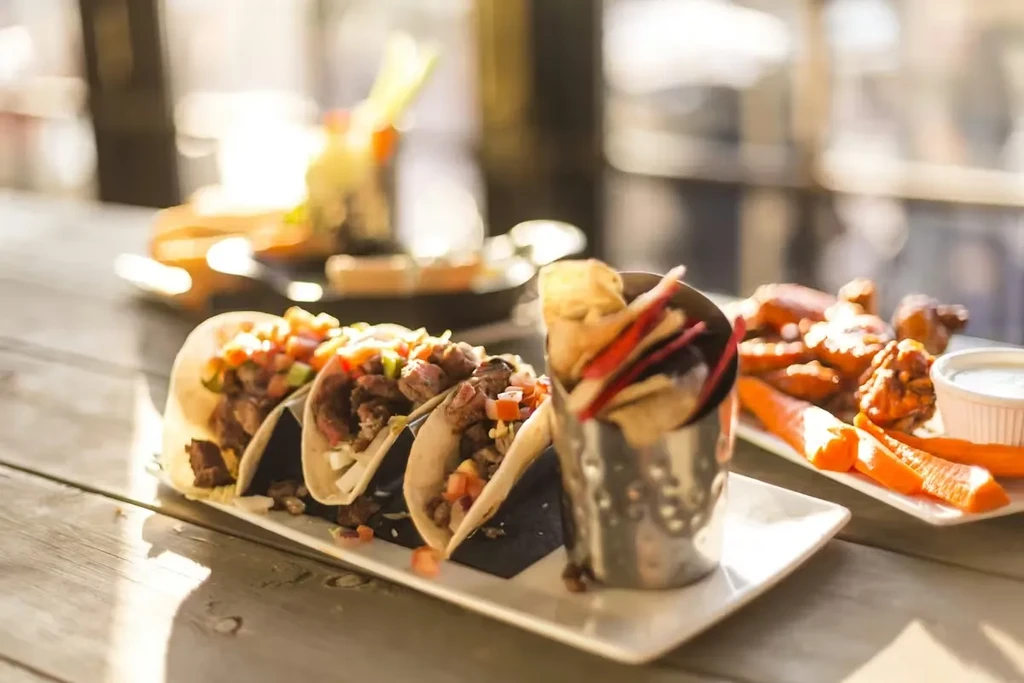 Close-up of tacos, fries, and chicken wings on a wooden table.