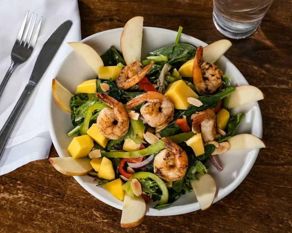 Shrimp, mango, and apple salad in white bowl on rustic table.
