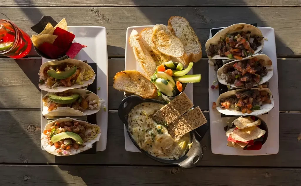 Overhead view of tacos, dip, bread, and drink on a wooden table.